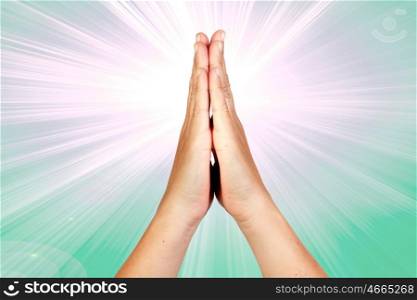 Hands clasped in prayer with rays of light on green background