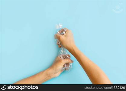 Hands crashing plastic bottles on blue background. Plastic utilisation concept. Attractive ecological problem positive poster.