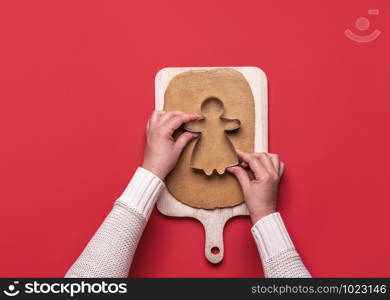 Hands cutting gingerbread dough with cookie girl-shaped cutter. Homemaking of Christmas gingerbread cookies. Traditional Xmas dessert preparation.