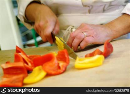 Hands cutting red and yellow peppers in kitchen.