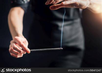 Hands holding a burning incense stick, black background. Incense Stick