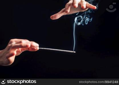 Hands holding a burning incense stick, black background. Incense Stick