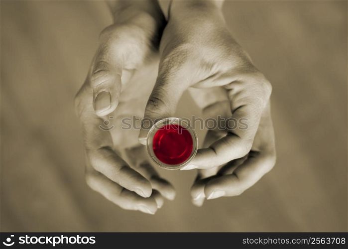 Hands holding a communion cup, the wine is red and the rest of the image is subdued color