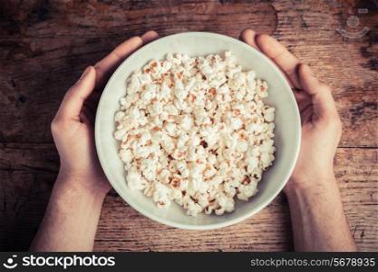 Hands holding a large bowl of popcorn on a wooden table