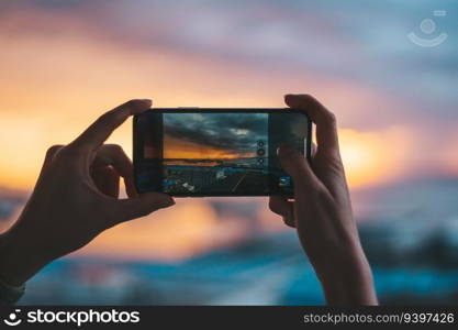 Hands holding a smartphone taking a photograph of the sea at sunset