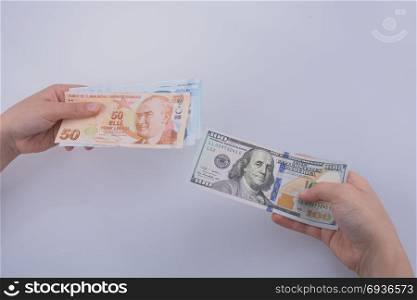 Hands holding American dollar banknotes and Turksh Lira banknotes side by side on white background