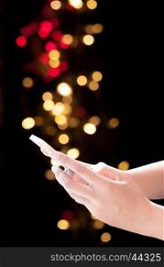 Hands holding mobile phone on Christmas background. Festive elegant background with bokeh lights and stars, copy space
