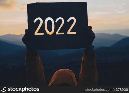 Hands holding of new year 2022 silhouette design from cardboard against the background of mountain with sunset. Happy New Year concept.