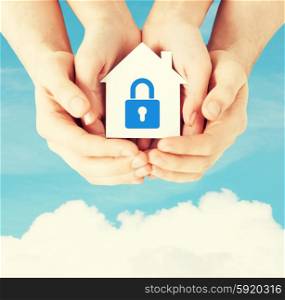 hands holding paper house with lock. real estate and family home security concept - closeup picture of male and female hands holding white paper house with blue lock