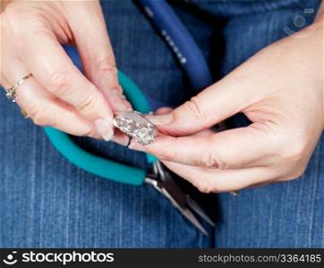 Hands holding pliers creating silver wire wrap pendant