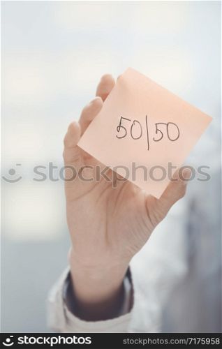 Hands holding sticky note with Fifty-fifty text