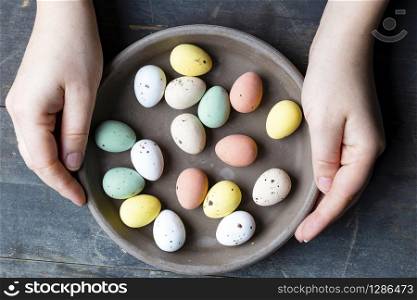Hands holding stylish pastel painted easter eggs in ceramic grey plate on vintage old wooden background, Happy Easter concept. Hands holding stylish pastel painted easter eggs in ceramic grey plate on vintage old wooden background, Happy Easter