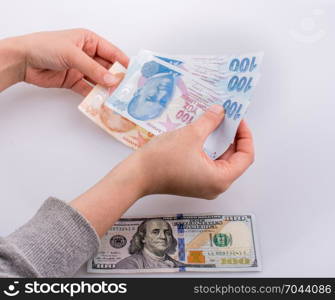Hands holding Turksh Lira banknotes by the side of American dollar banknotes on white background