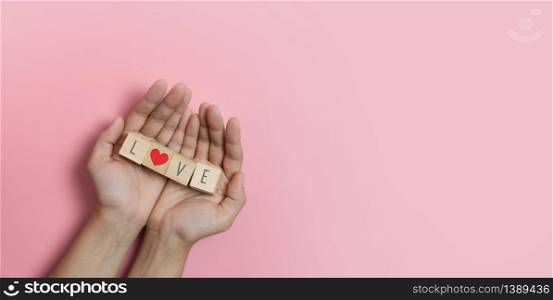 Hands holding Wood cubes with Love text and red heart on pink background. Valentines day, Love concepts.