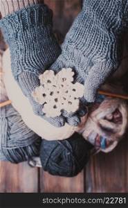 Hands in a grey gloves holding white knitted snowflake as a winter symbol. Hands in knitted gloves