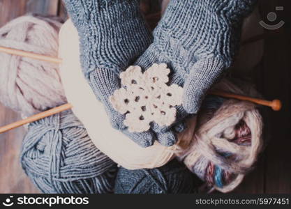 Hands in a grey gloves holding white knitted snowflake as a winter symbol. Hands in knitted gloves