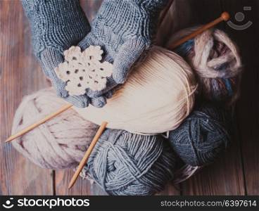 Hands in a grey gloves holding white knitted snowflake as a winter symbol. Hands in knitted gloves