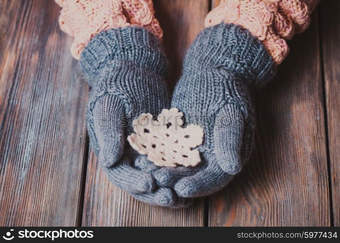 Hands in a grey gloves holding white knitted snowflake on a wooden background. Close-up hands in glove