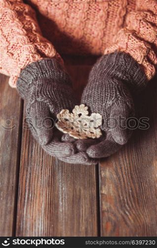 Hands in a grey gloves holding white knitted snowflake on a wooden background. Close-up hands in glove