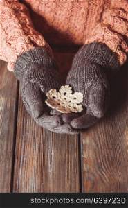 Hands in a grey gloves holding white knitted snowflake on a wooden background. Close-up hands in glove