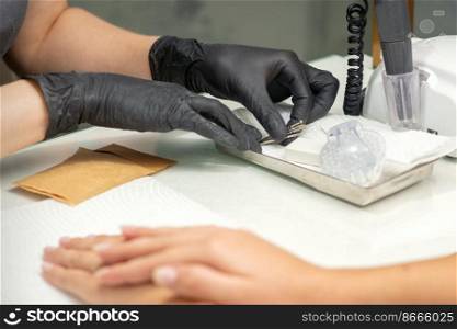 Hands in black gloves of manicurist preparing special nail file equipment for manicure treatment in a beauty salon. Hands in black gloves of manicurist preparing special nail file equipment for manicure treatment in a beauty salon.
