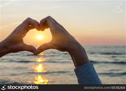 Hands in heart shape framing sun. Hands and fingers in heart shape framing setting sun at sunset over ocean