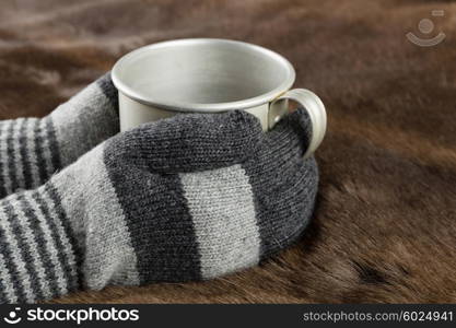 Hands in knitted gloves keep aluminum mug