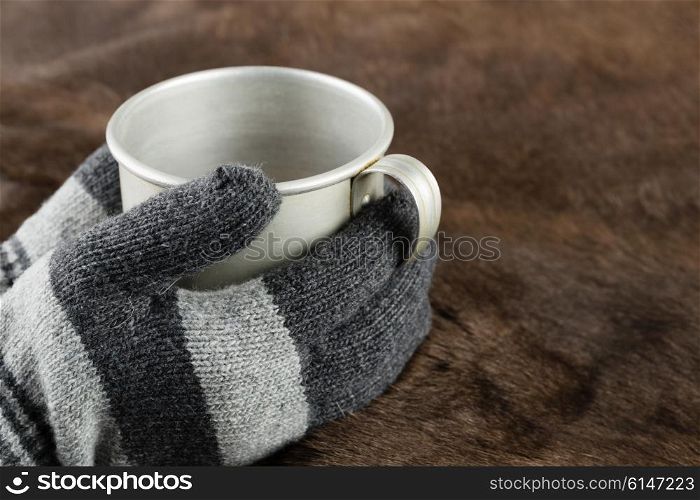 Hands in knitted gloves keep aluminum mug