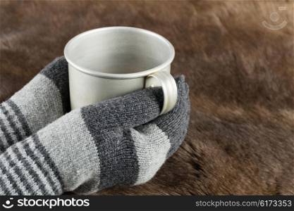 Hands in knitted gloves keep aluminum mug