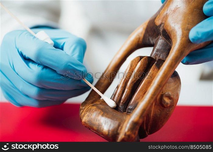 Hands in protective gloves cleaning and preparing wood sculpture for repair and restoration. Cleaning and Preparing Wood Sculpture for Repair