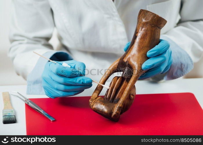 Hands in protective gloves cleaning and preparing wood sculpture for repair and restoration. Cleaning and Preparing Wood Sculpture for Repair