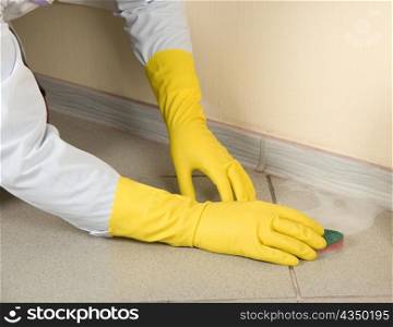 Hands in yellow gloves with sponge, washing floor and plinth
