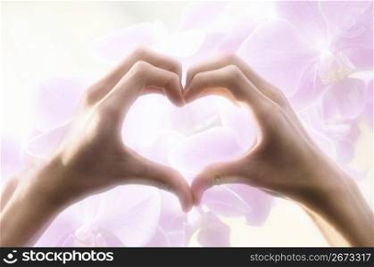 Hands making a heart shape with a flowered background