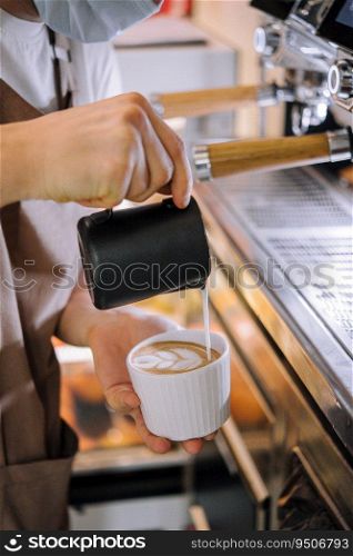 Hands of a barista pouring warm milk into a cappuccino or latte