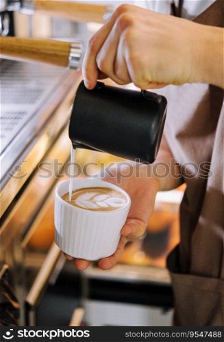 Hands of a barista pouring warm milk into a cappuccino or latte