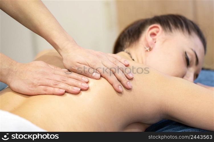 Hands of a masseur woman on the back of a young girl. Advertising spa or massage parlor. Hands of a masseur woman on the back of a young girl