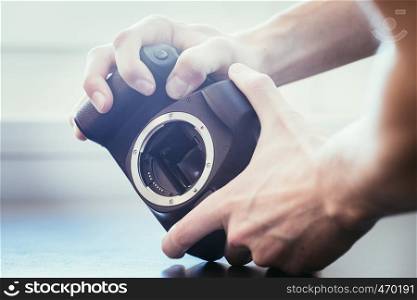 Hands of a photographer are touching a professional reflex camera, open sensor
