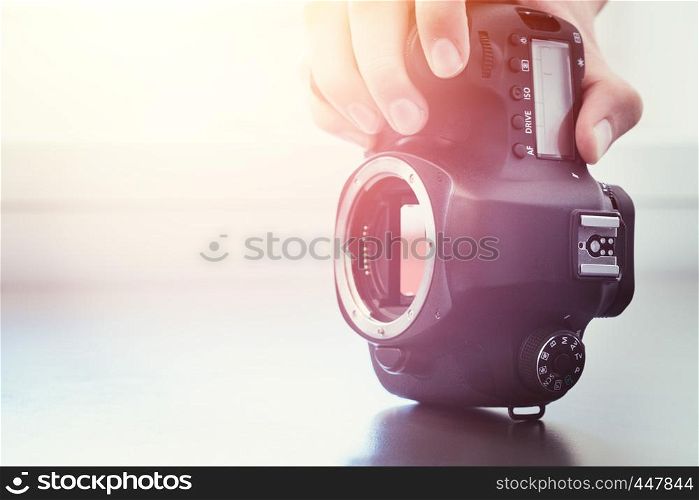 Hands of a photographer are touching a professional reflex camera, open sensor. Sunlight.