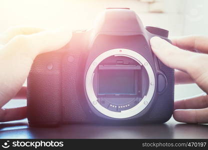 Hands of a photographer are touching a professional reflex camera, open sensor. Sunlight.