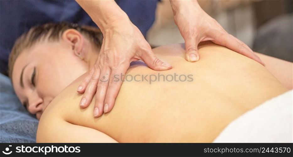 Hands of a woman masseur make therapeutic massage on the back of a young girl. Advertising a beauty salon or massage room treatment room. Hands of a woman masseur make therapeutic massage on the back of a young girl