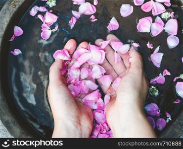 Hands of a young woman, bright petals of roses and old, copper basins with water. Top view, close-up. Beauty and body care concept. Hands of a woman, petals of roses
