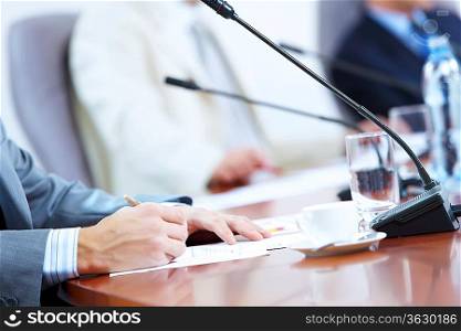 Hands of businessman writing with pen at conference against defocused background