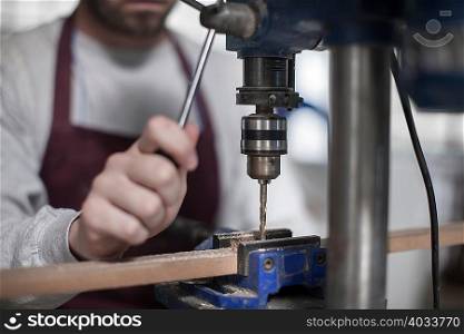 Hands of carpenter adjusting drilling machine in workshop
