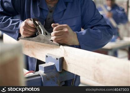 Hands of carpenter using planer on plank in workshop
