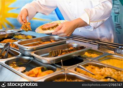 Hands of cook putting in plate vegetable ragout in public catering restaurant