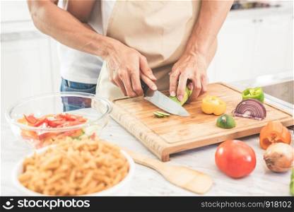 Hands of couple or lovers cooking and slicing vegetables with knife together. Man teaching woman to cook. Happiness in holiday and honeymoon concept