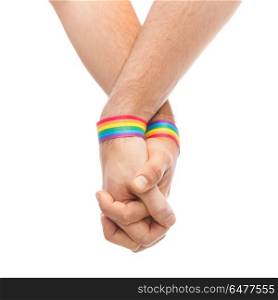 hands of couple with gay pride rainbow wristbands. lgbt, same-sex relationships and homosexual concept - close up of male couple wearing gay pride rainbow awareness wristbands holding hands