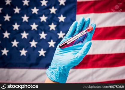 Hands of doctor wearing gloves holding blood test tube coronavirus  COVID-19  virus in the laboratory on flag United States of America background, USA Vaccination