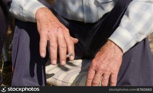 Hands of elderly homeless man smoking a cigarette
