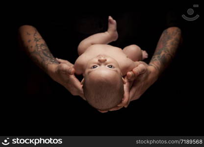 Hands of Father and Mother Hold Newborn Baby Under Dramatic Lighting Against A Black Background.